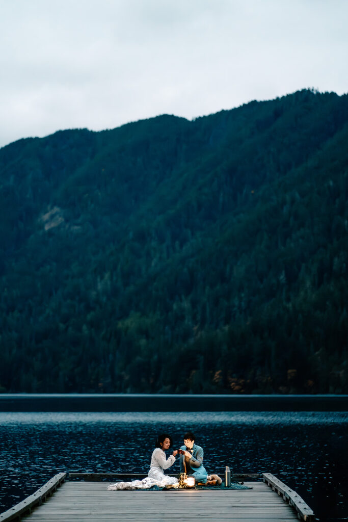 a couple in their wedding attire sit dockside during blue hour, sharing tea together after exploring one of the best places to elope in Washington