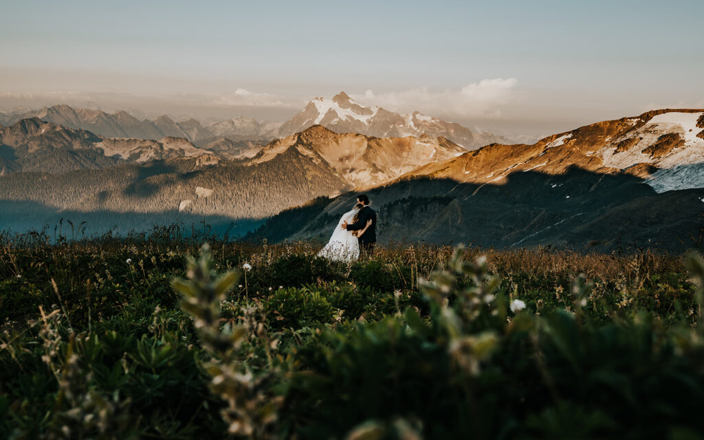 a couple in wedding attire embrace and take in the mountain landscape around them as they explore one of the best places to elope in Washington