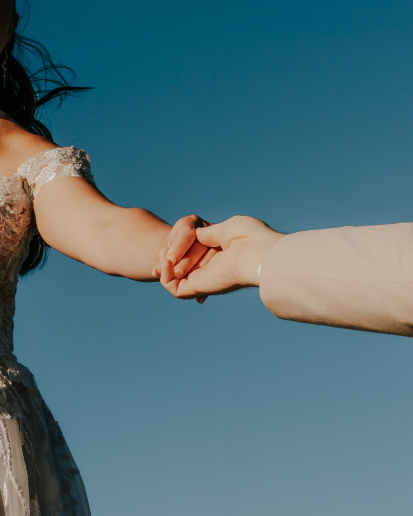a shot of a couples hands reaching towards each other. A punchy blue sky serves as the background 