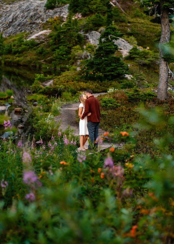 a bride and groom share a passionate kiss in a wildflower meadow. the foreground of the image is smattered with pops of color from the wildflowers that surround them. 