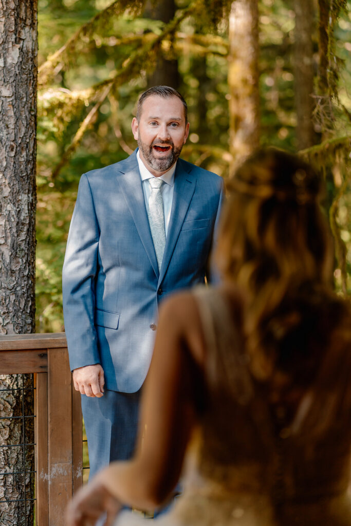 a grooms jaw drops down as he sees his bride for the first time in her wedding dress. the shot is taken from over her shoulder and we have her perspective of the moment. 