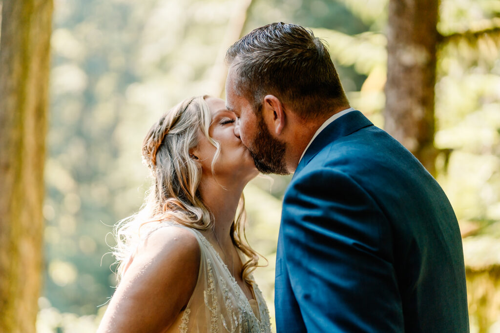 a bride and groom in their wedding attire kiss under dappled lighting after sharing a first look during their mt baker micro wedding 