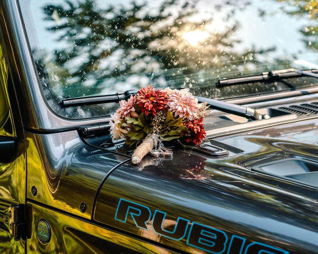 a colorful pink bouquet rests on the hood of a rugged jeep. we see that the windshield is dirty from recent adventures leading up to this mt baker micro wedding day 