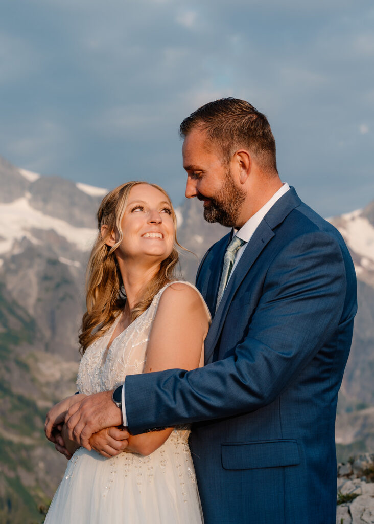 a groom wraps his arms around his bride as she stands in front of him. she grins widely as she looks back at him overcome with joy and love from their mt baker micro wedding 