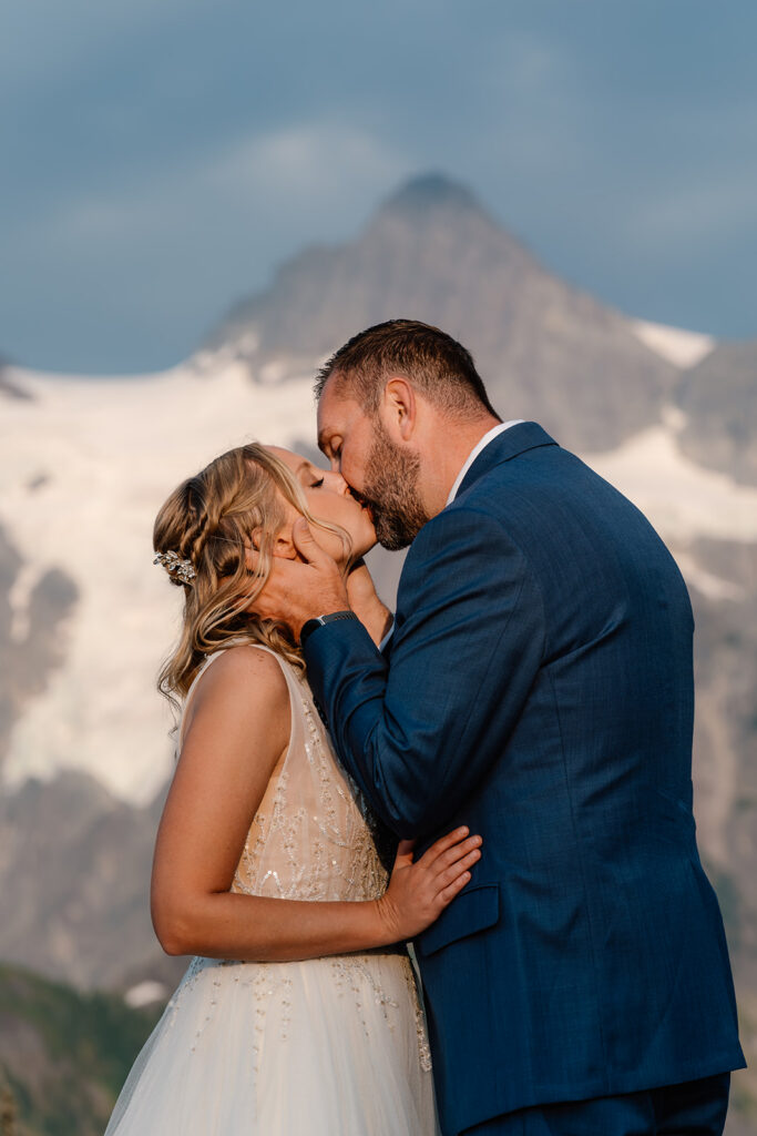 a bride and groom share a passionate kiss in front of a staggering mountain 