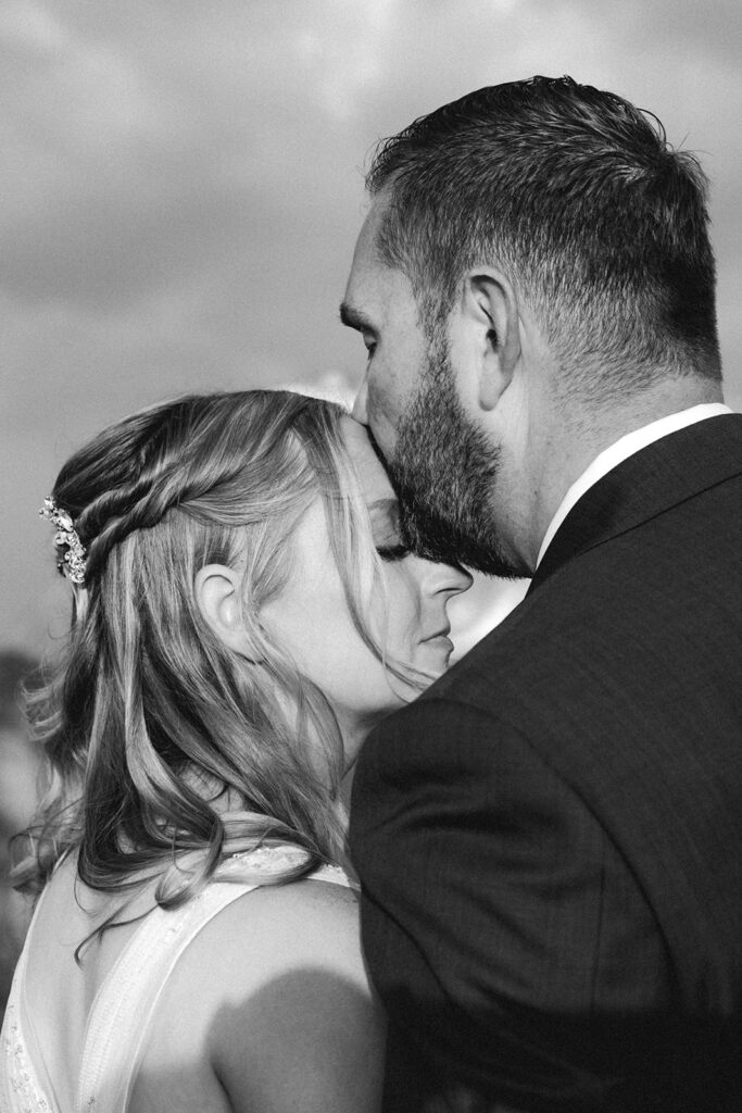 a tender moment of a groom kissing the forehead of his bride 