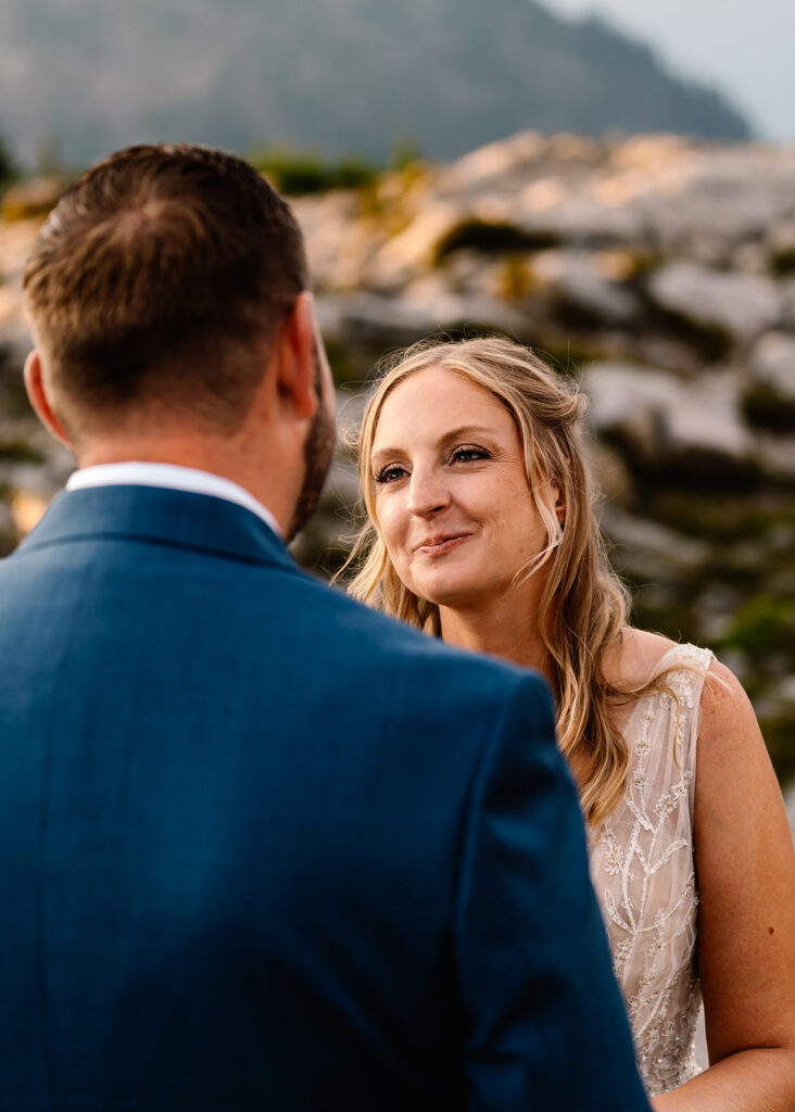 shot over the grooms shoulder, we see his bride smiling sweetly at him. She is radiating joy and deep love 