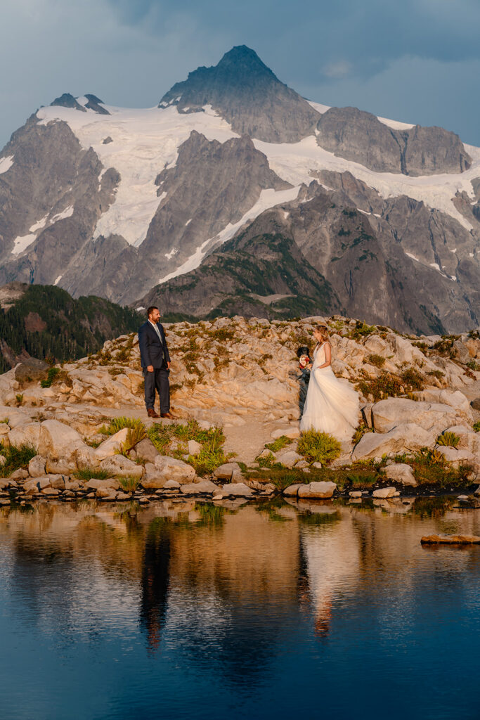 a bride swishes her wedding dress for her groom. mountains rise behind them as they gaze at each other during their mt baker micro wedding 