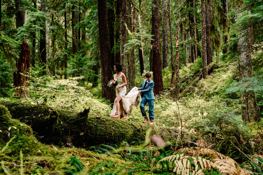 a couple in their wedding attire walk on a mossy log in the middle of a mossy forest during their hoh rainforest elopement 