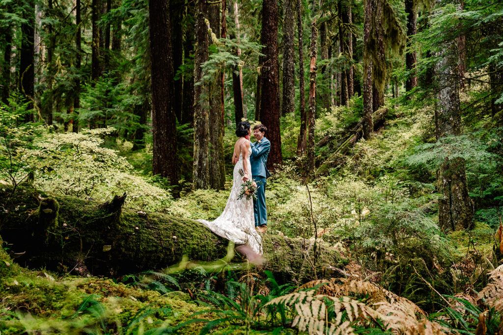 a couple in their wedding attire embrace on a mossy log in the middle of a mossy forest during their hoh rainforest elopement 