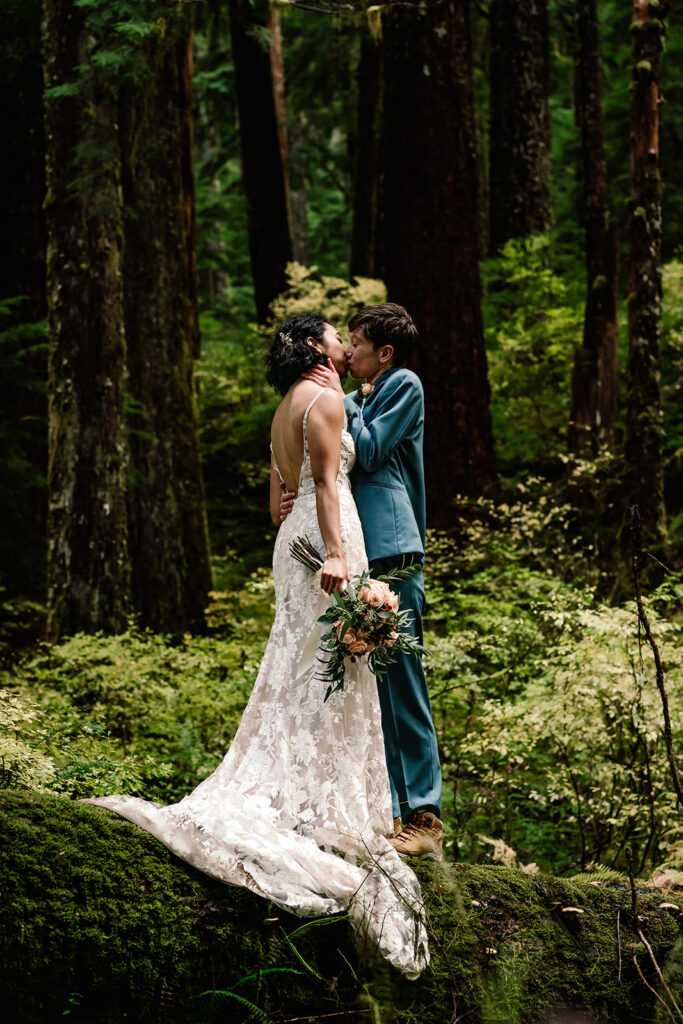 a couple in their wedding attire embrace on a mossy log in the middle of a mossy forest during their hoh rainforest elopement 