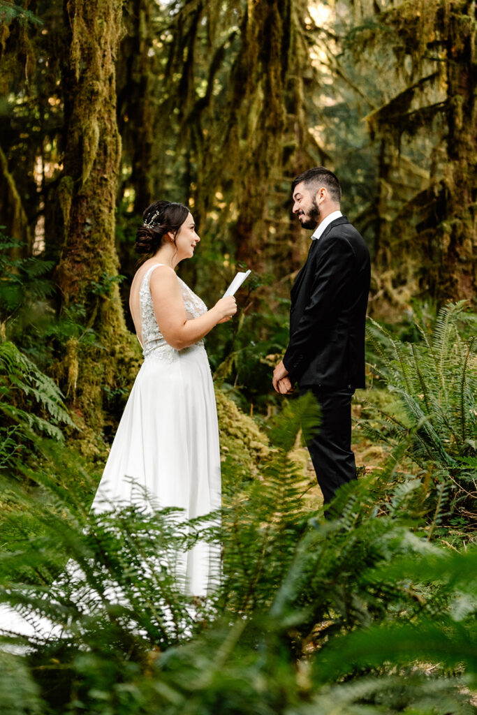 a couple in their wedding attire exchange vows surrounded by lush ferns and hanging moss during their hoh rainforest elopement