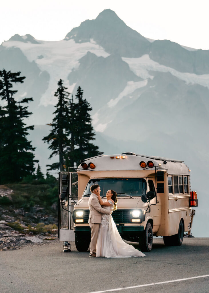 a bride holds the face of her groom in her hands after they exchange a first look in front of their bus (that is also their home on wheels) moutains rise behind them during their artist point elopement 