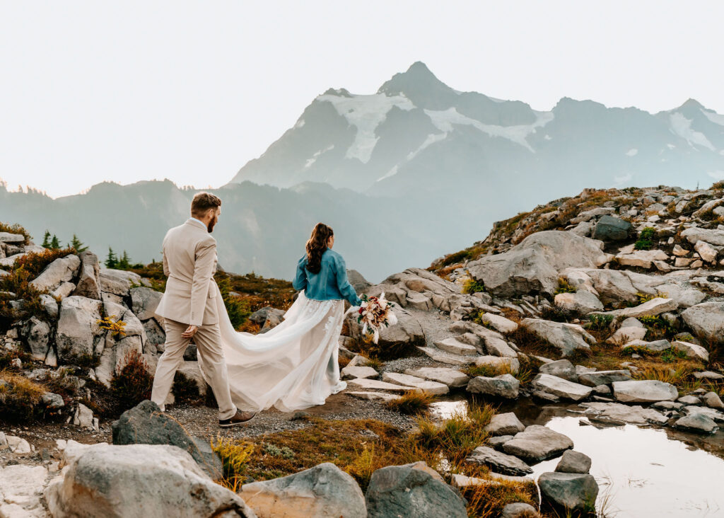 a bride and groom hike the rocky terrain in their wedding attire as they explore, looking for the perfect ceremony spot for their artist point elopement 