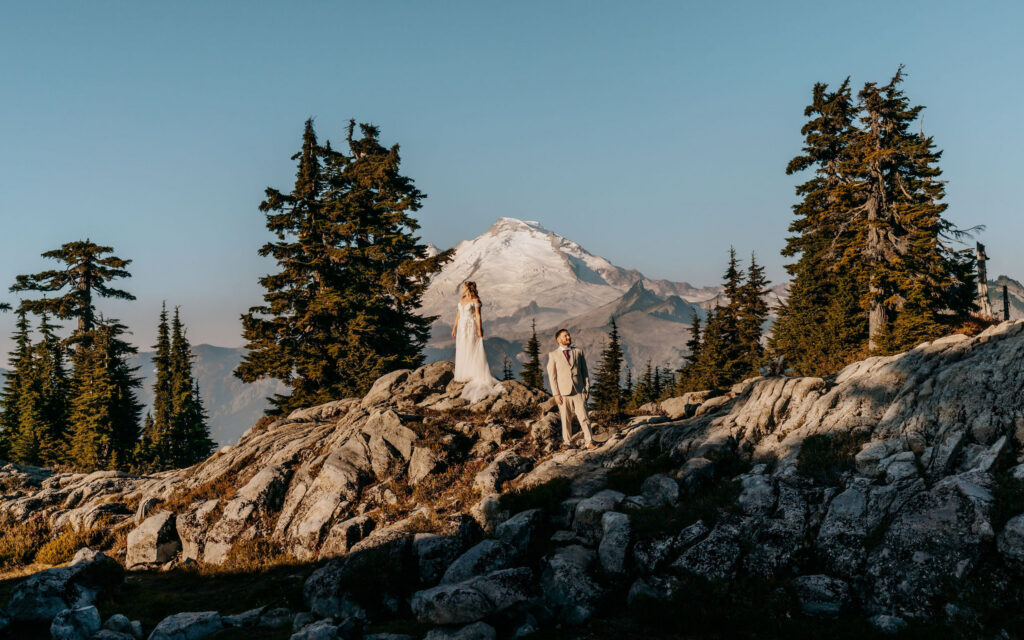 a couple, in their wedding attire pose in front of a stunning mt baker as the sun rises in the sky during their artist point elopement 
