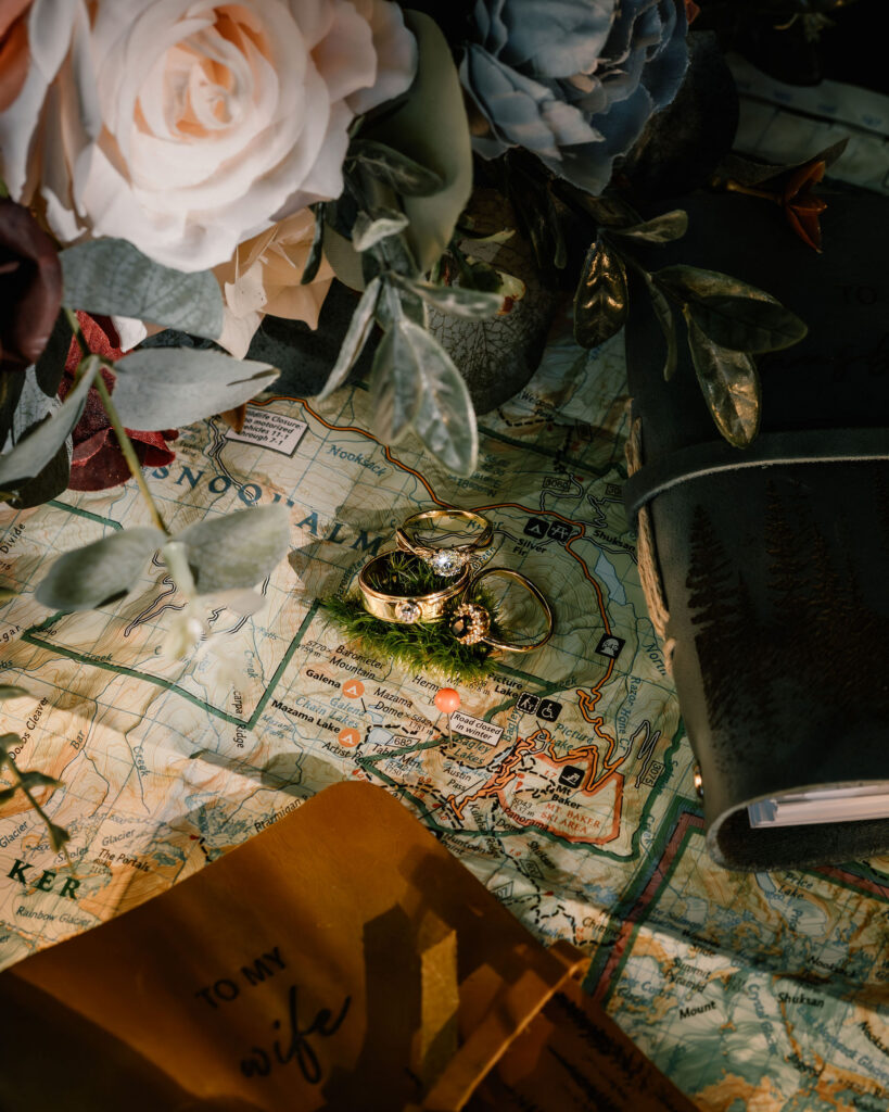 a close up shot of the details from this artist point elopement. We see their rings clustered together, vow books and flowers paint the edges 