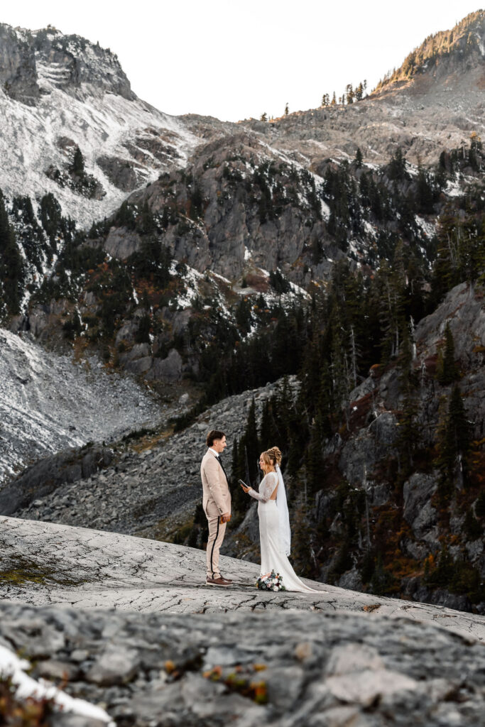 an image of a bride and groom exchanging vows during their artist point elopement. The terrain is rocky and beautiful. Snow speckles the mountains behind them and golden light paints the top