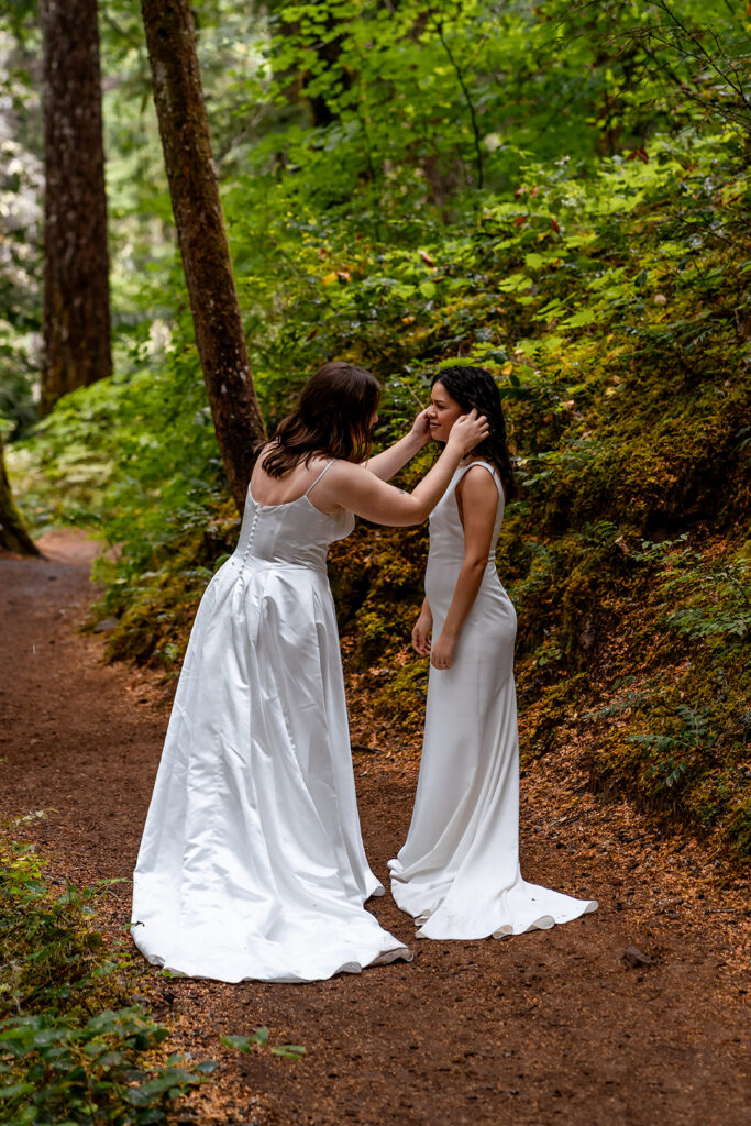 a bride fixes her brides hair as they explore a wooded trail