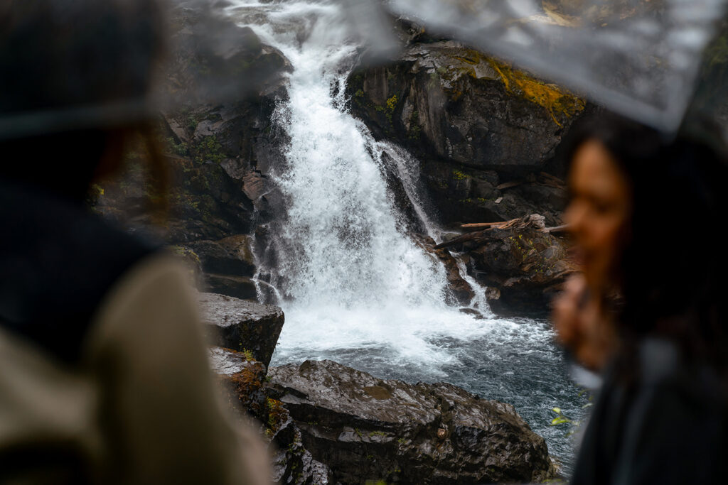 two brides frame a shot of a gushing waterfall in front of them 