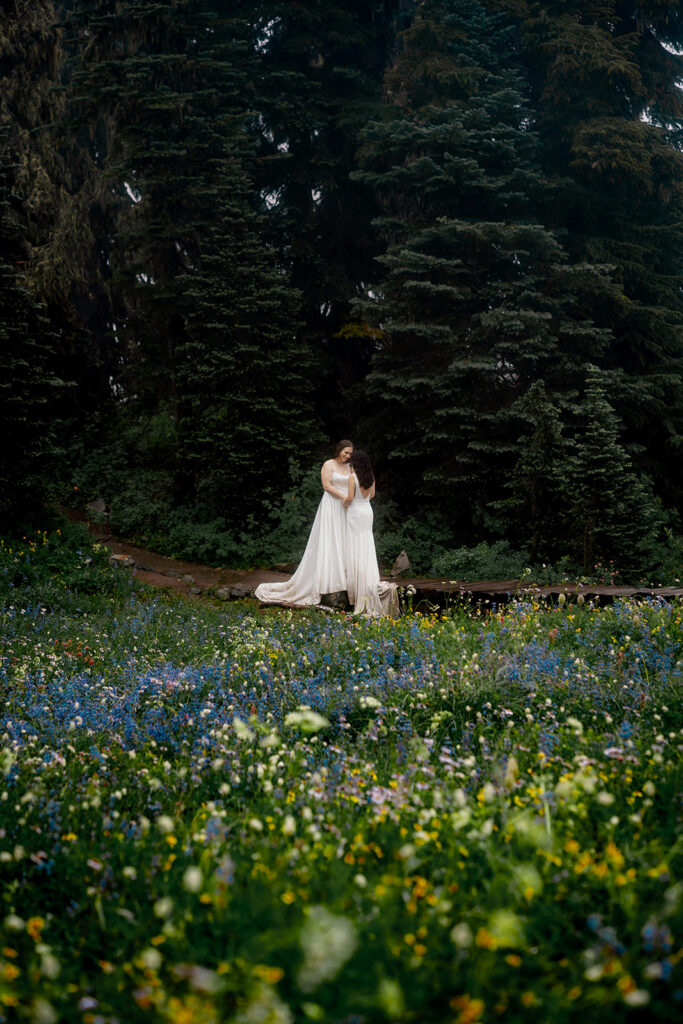 two brides embrace in a field of wildflowers during their tipsoo lake elopement 