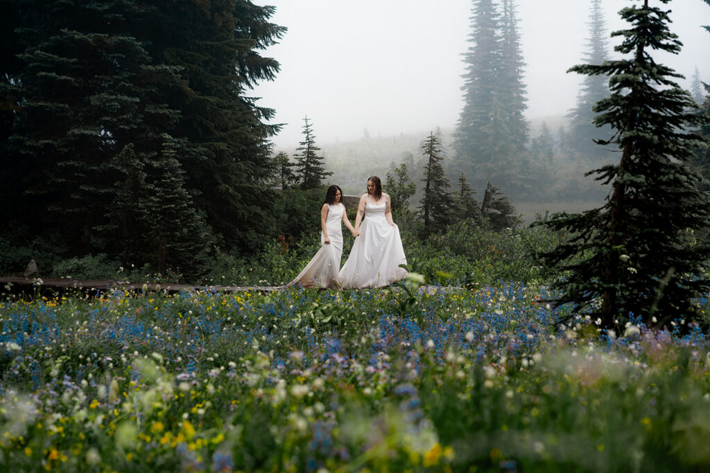 two brides wander through a field of wildflowers in a foggy landscape during their tipsoo elopement 