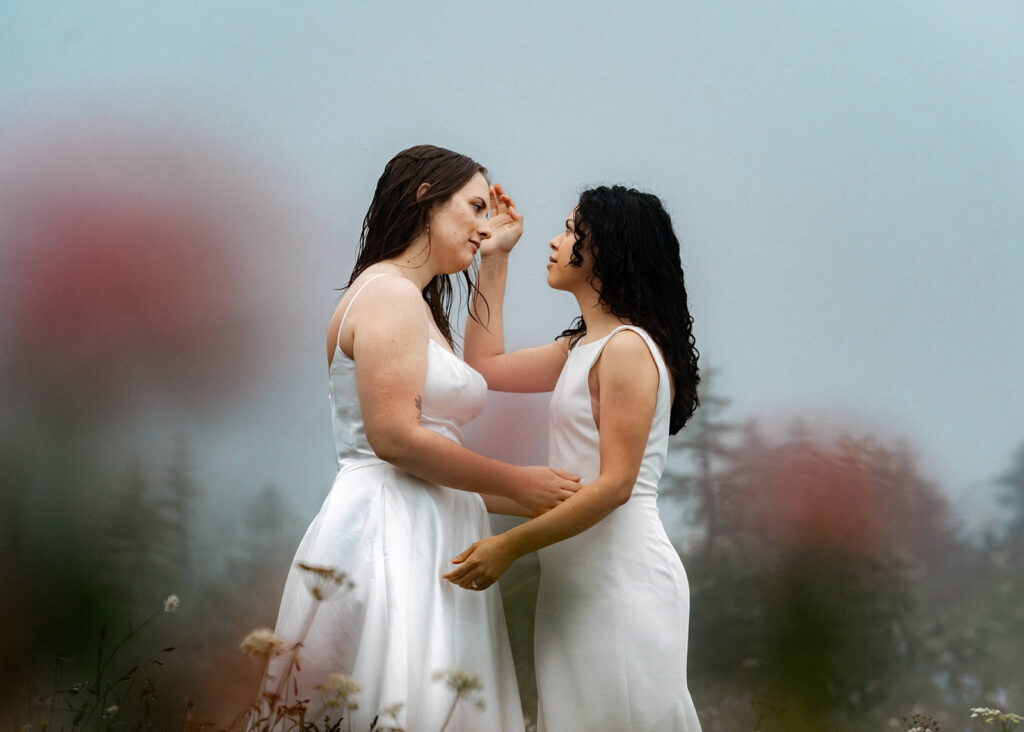 a bride fixes the hair of her bride as they are framed by pink wildflowers 