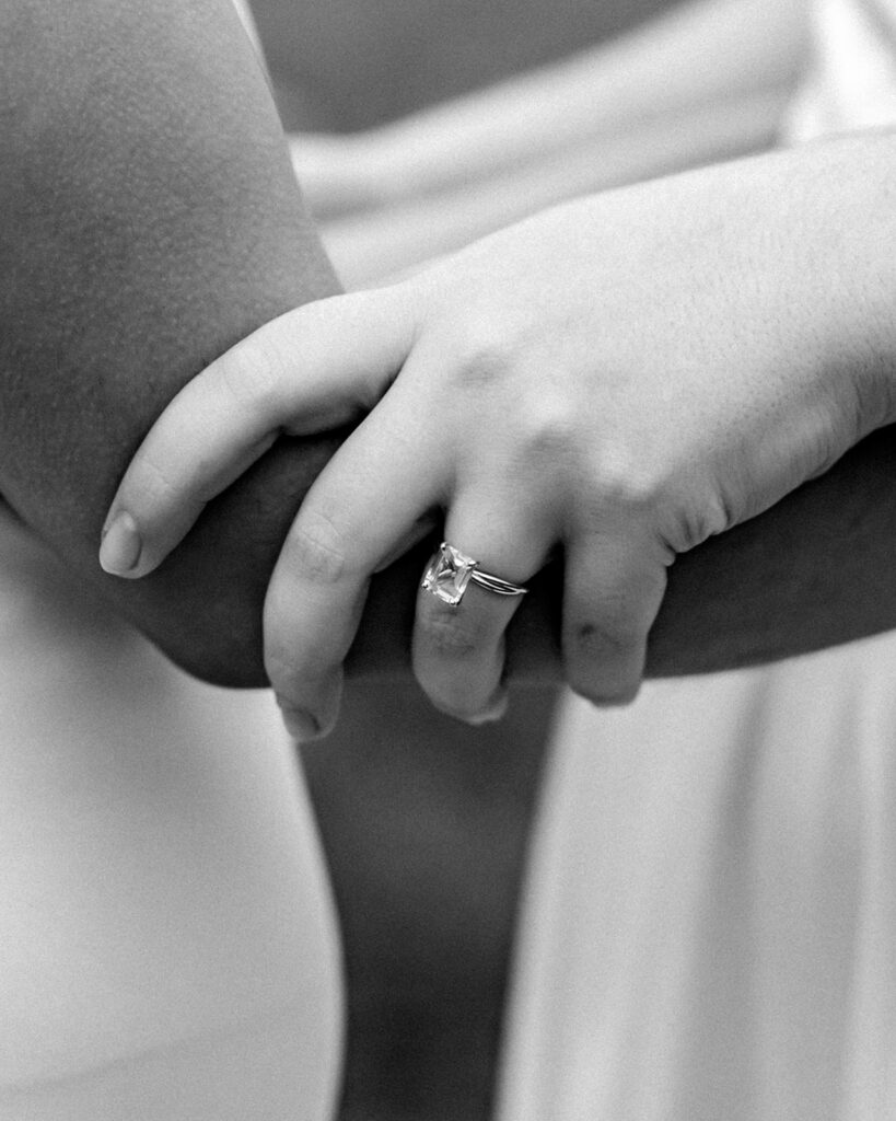 a close up shot of hands embracing and a square cut wedding ring 
