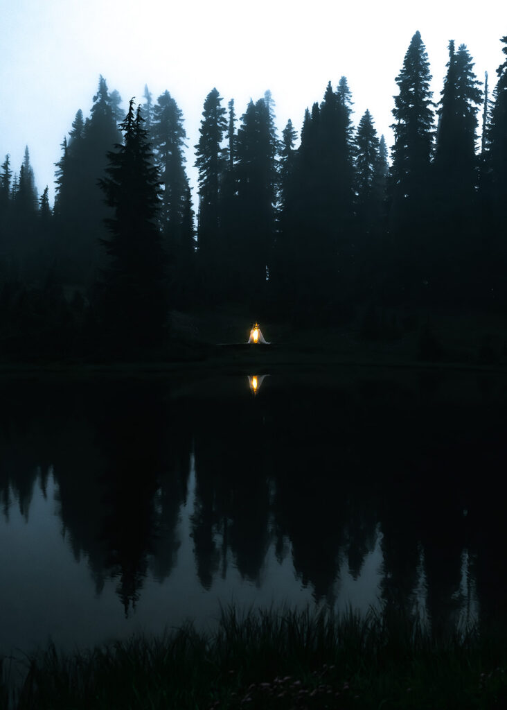 two brides lit by lanterns in a foggy landscape. They are reflected back in the still lake during the tipsoo lake elopement 