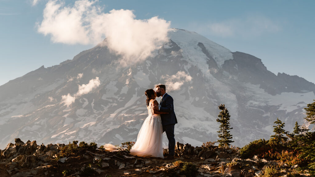 a couple in wedding attire kiss in front of a massive mount rainier. 