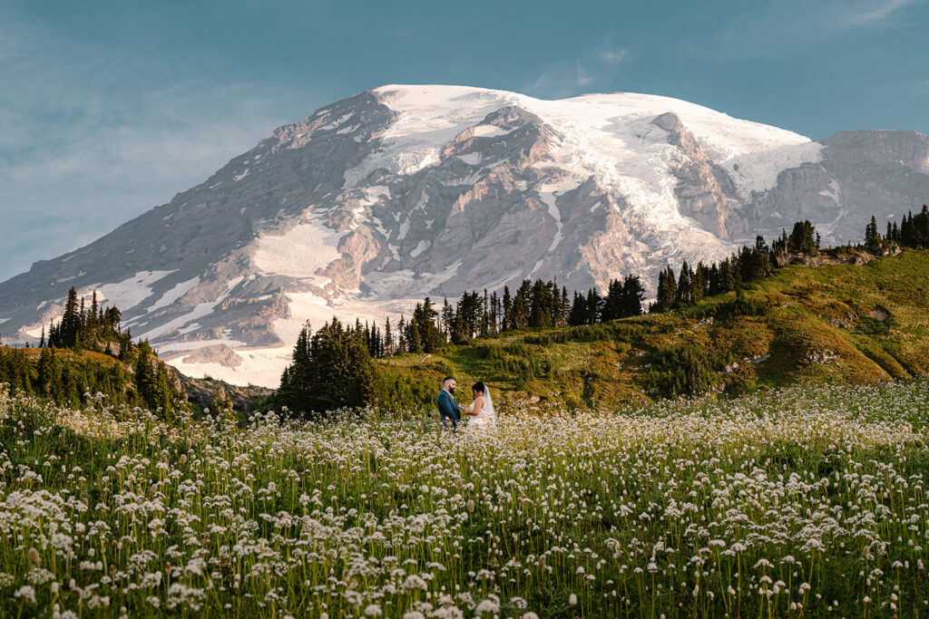a bride and groom share vows in a field of wildflowers with mount rainier rising behind them