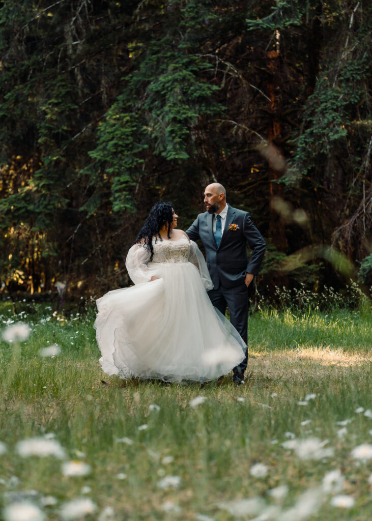 a bride and groom gaze lovingly at each other in the soft morning light of a spring day. The foreground is framed by soft and blurry wildflowers