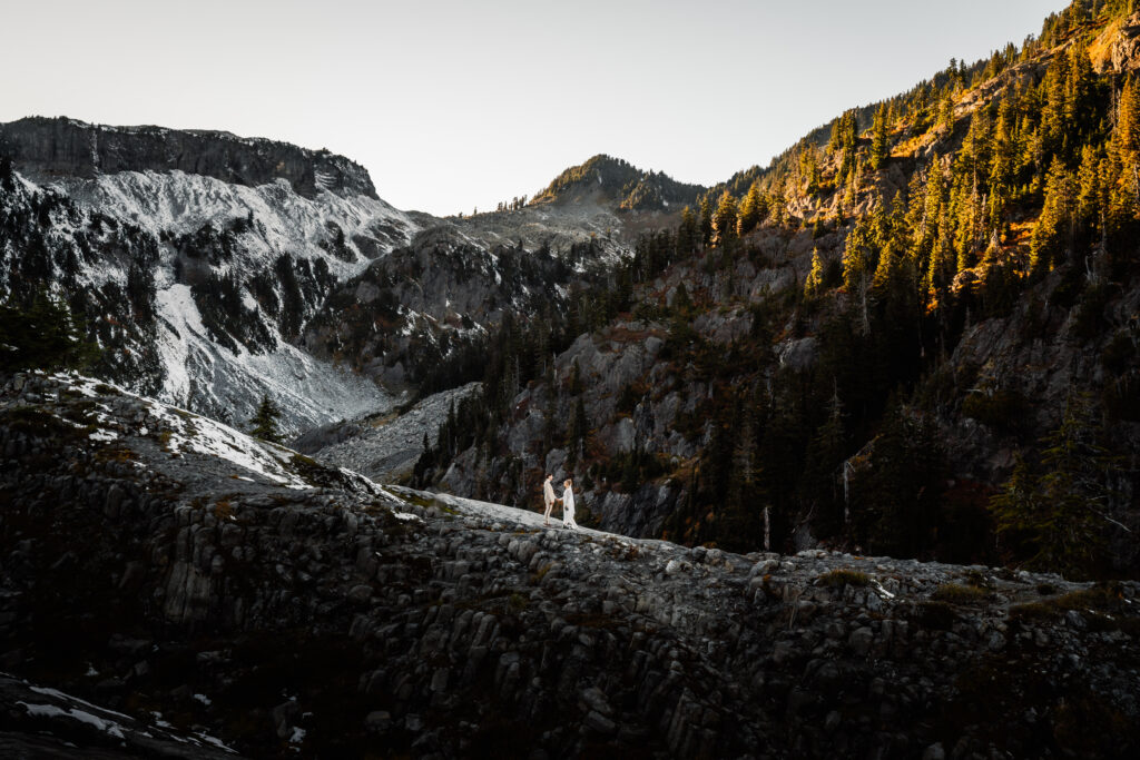 a fall elopement where we see a mountain landscape dusted lightly with snow. perfectly centered under the peak of a mountain, we see a bride and groom holding hands