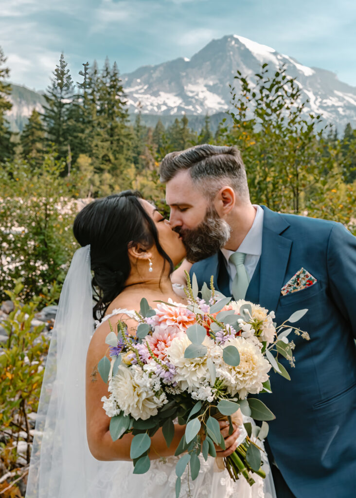a bride and groom share a kiss with rainier in the background