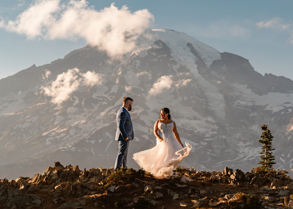 a bride twirls her dress in front of a massive mount rainier. the sunlight highlighted in the fabric of her dress