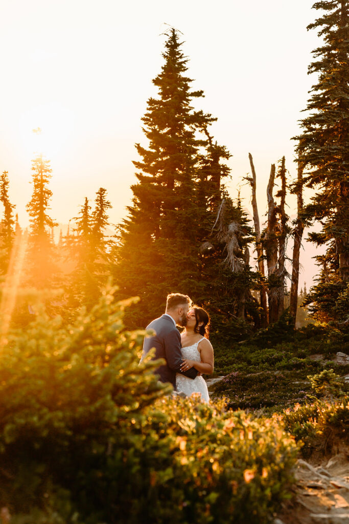 a bride and groom kiss on the trail as golden sunlight fills the frame with a burst.