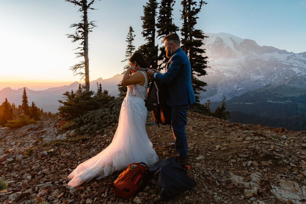 a groom helps his bride secure her pack as they begin to hike back
