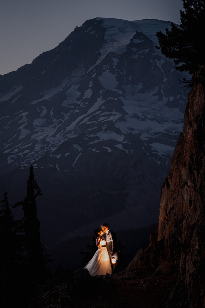 a bride and groom kiss under the view of rainier. It is dusk now and the only light that remains is the subtle blue glow of the mountain and the warm light of their lanters