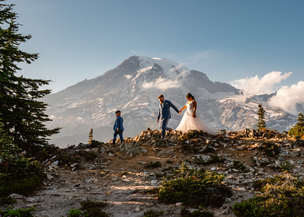 a bride and groom in their wedding attire explore a rocky out cropping with their young sun leading the way