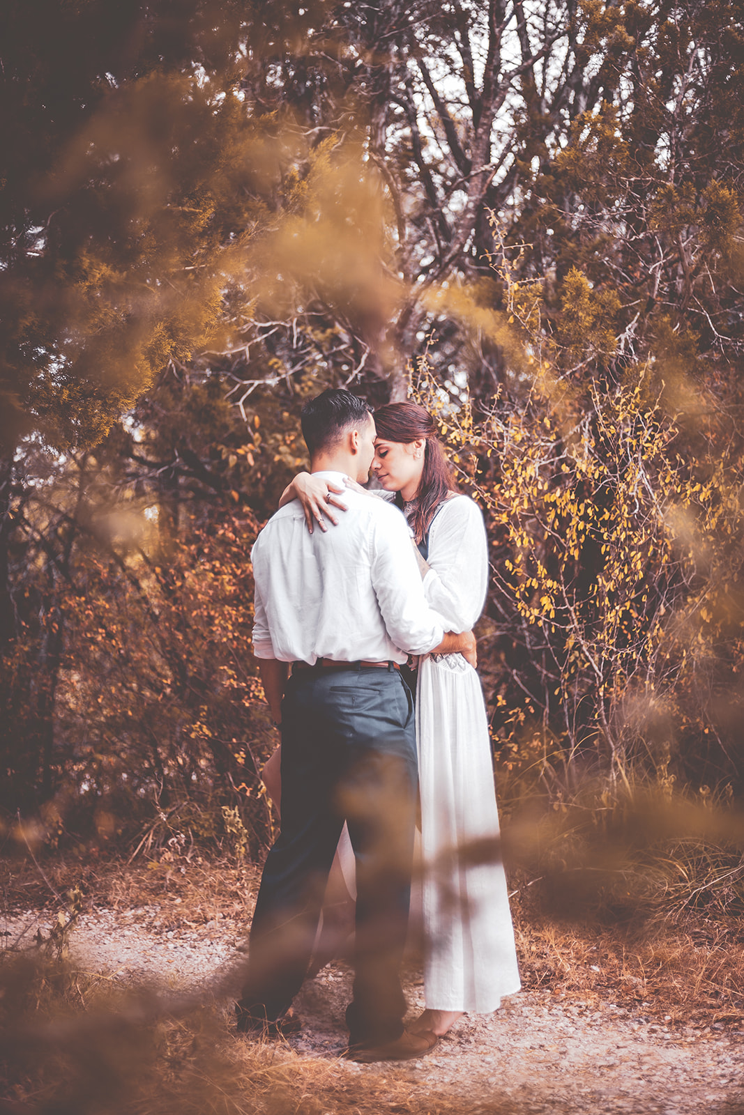A Texas couple in wedding attire snuggling under autumn branches after their elopement