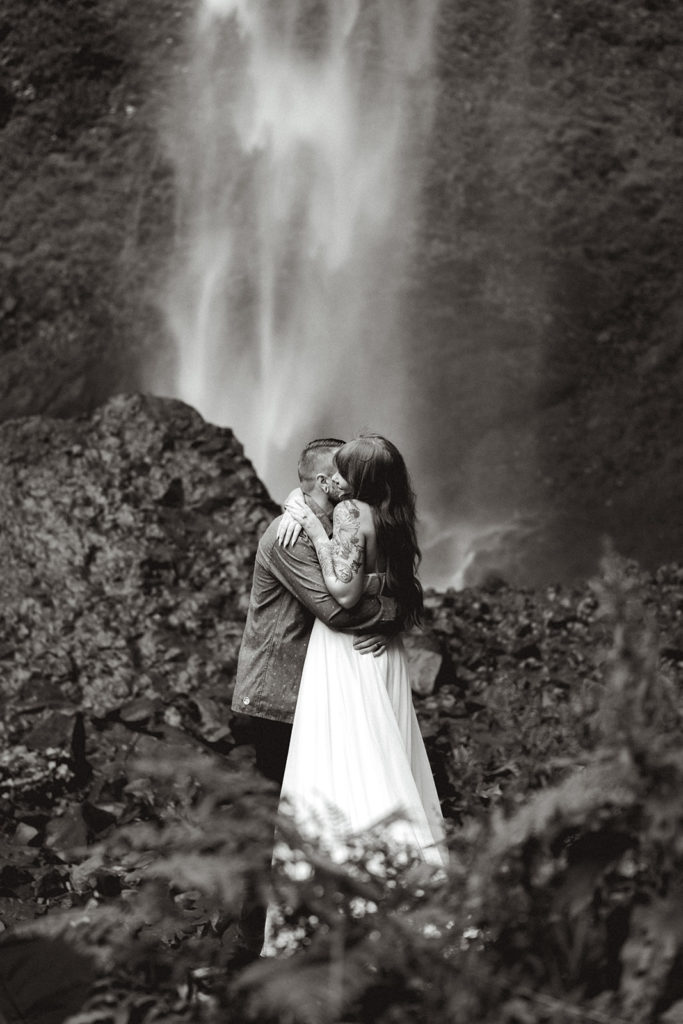 Bride and groom embrace in front of gushing waterfall during their waterfall elopement. 