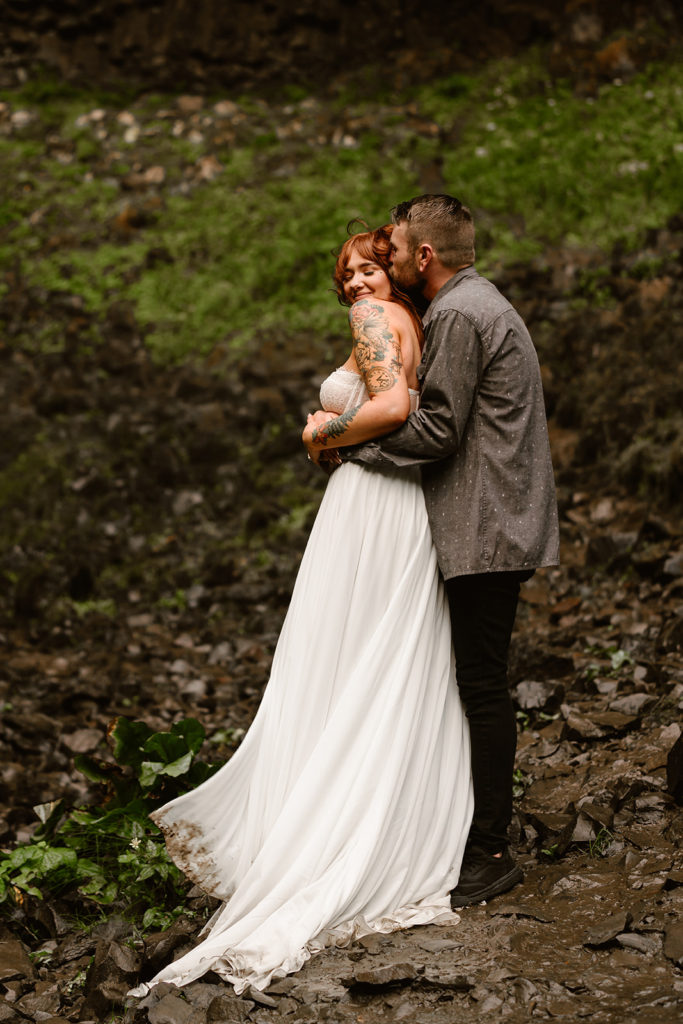 Bride and groom embrace in their wedding attire during their waterfall elopement.