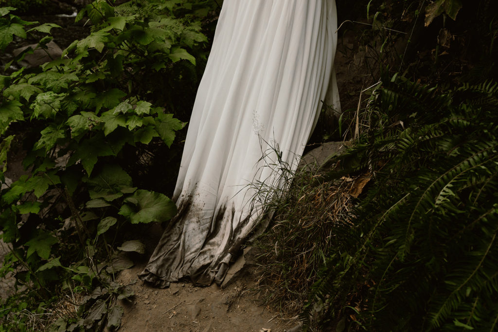 Shot of brides dirty dress dragging through mud and greenery during waterfall elopement.