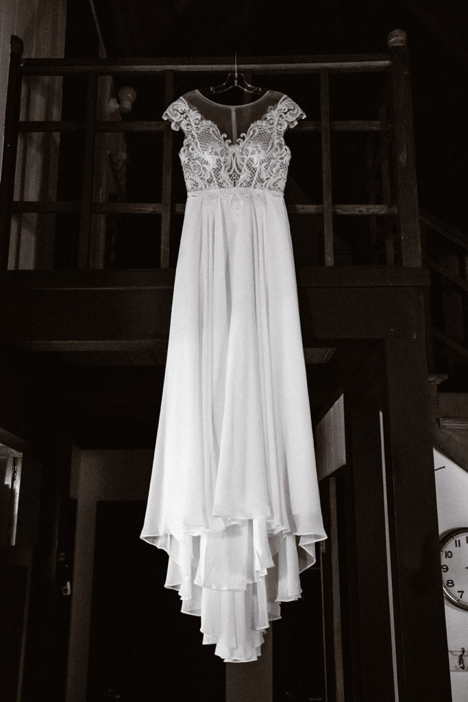 Black and white photo of a wedding dress hanging from the balcony of a wooden staircase during a mt rainier wedding day