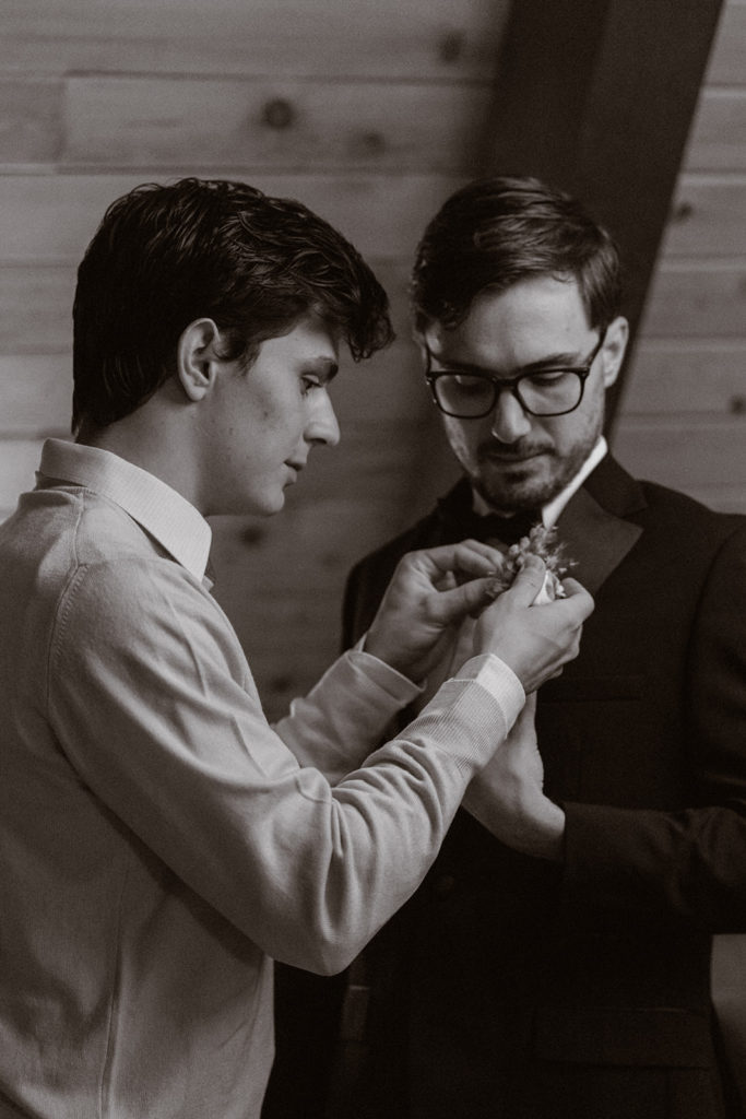 Black and white photo of a groom and his brother getting ready in their cabin during his Mt. Rainier wedding.