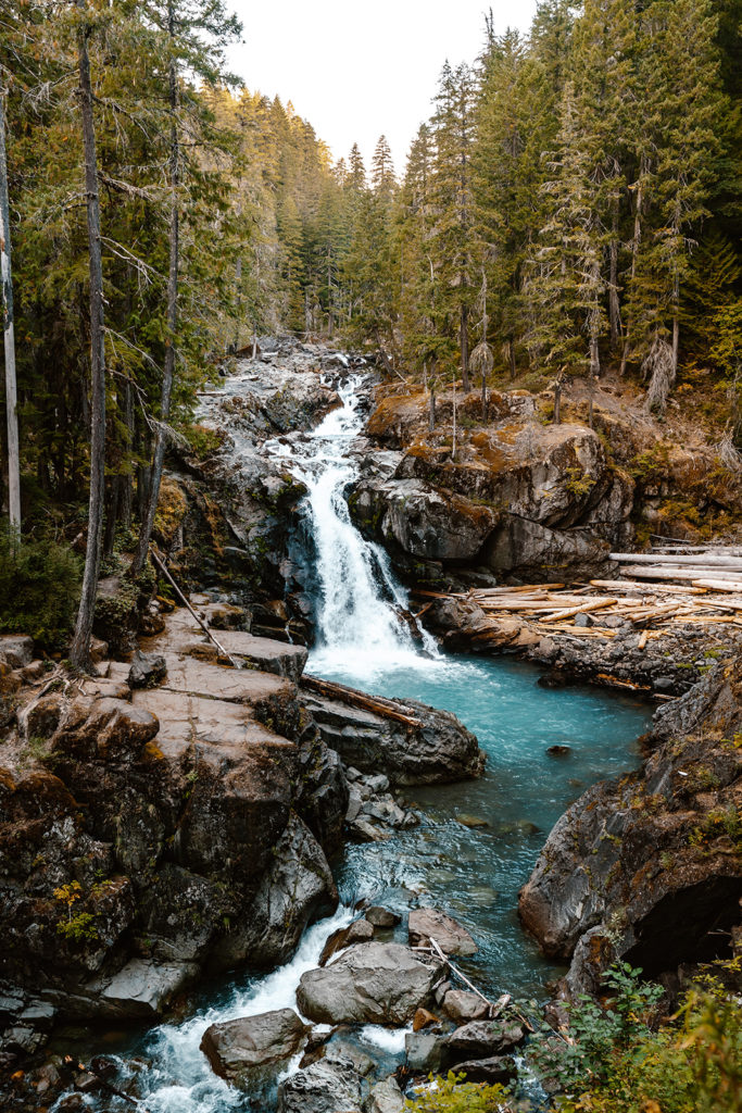 turquoise waterfall surrounded by pines and jagged cliffs, serving as the perfect location for a mt. rainier wedding 