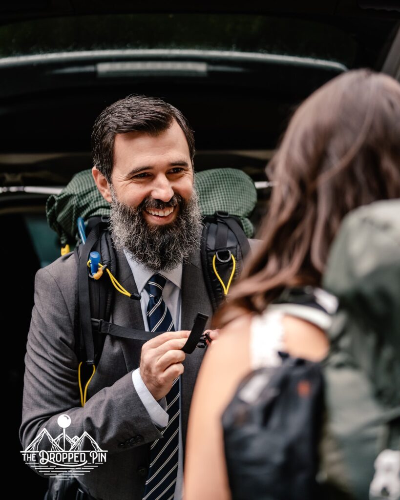 A groom smiles at his bride as they put on their camping packs preparing for an adventurous Washington elopement
