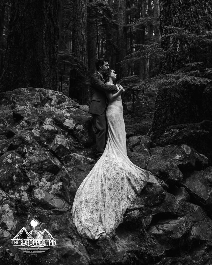 A couple stands on top of a jagged boulder looking out into the forest during their Washington elopement