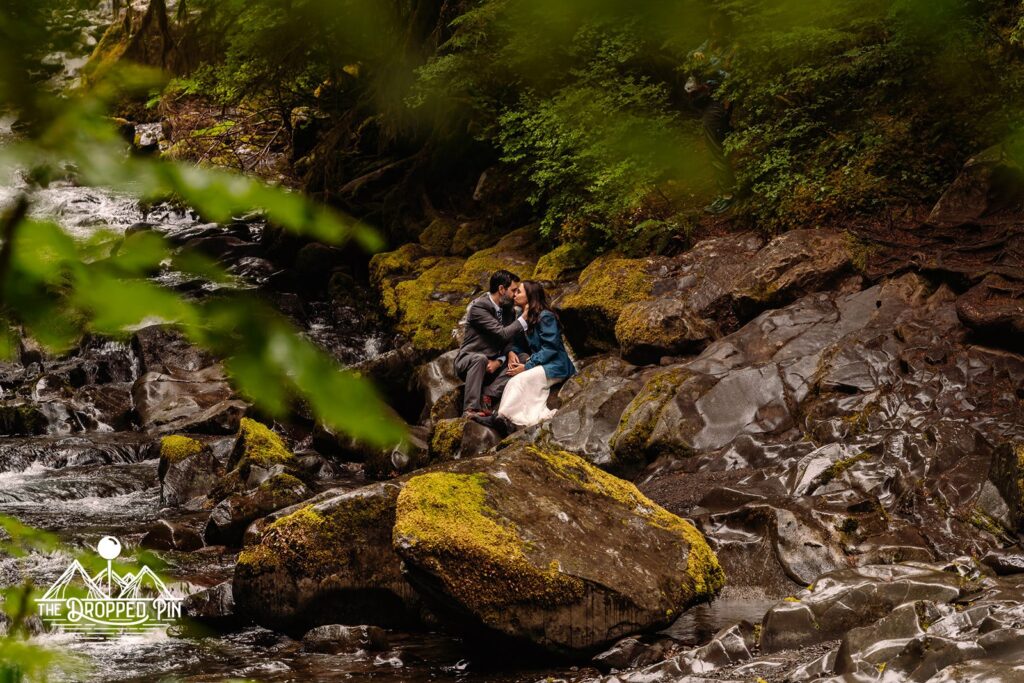 Couple sits on the rocks of a riverbed in wedding attire sharing vows during their Washington Elopement