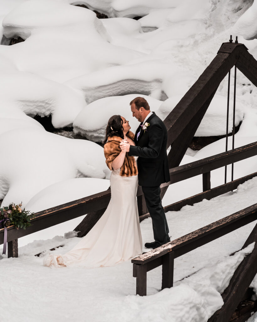 during their elopement timeline, a couple in wedding attire dances inn the snow.