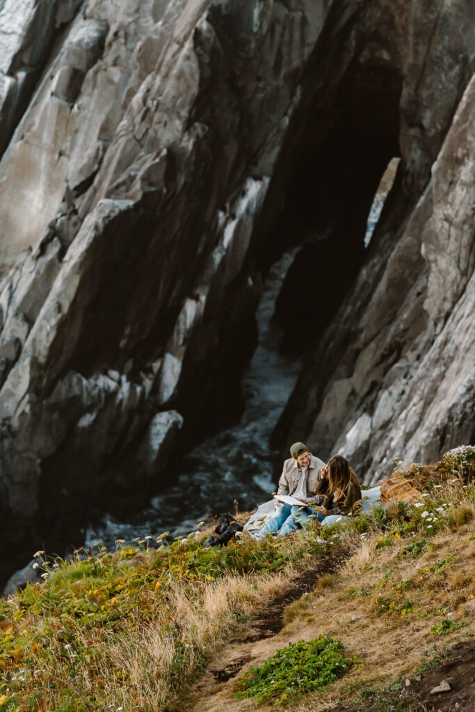 during the morning of their coastal elopement, a bride and groom read a book together on an ocean cliffside. 